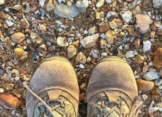Person,wearing,walking,boots,standing,on,a,pebble,beach,with