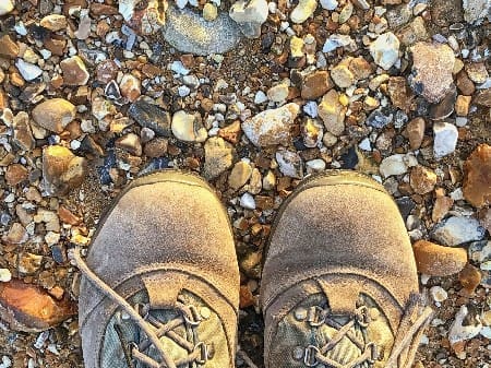 Person,wearing,walking,boots,standing,on,a,pebble,beach,with