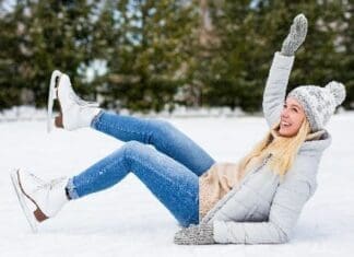 Embarrassed Young Woman Falling Down While Ice Skating At Winter Rink